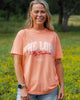 Woman wearing a peach-colored t-shirt with text in a field