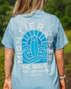 Person wearing a light blue t-shirt with a graphic design and text outdoors.