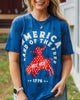 Woman wearing a blue t-shirt with a graphic design, standing outdoors near a building.